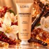 Jasnobeżowa tubka kremu do rąk Loris Frequence Spicy Flower K284 wśród jasnych kwiatów i złocistych dekoracji.